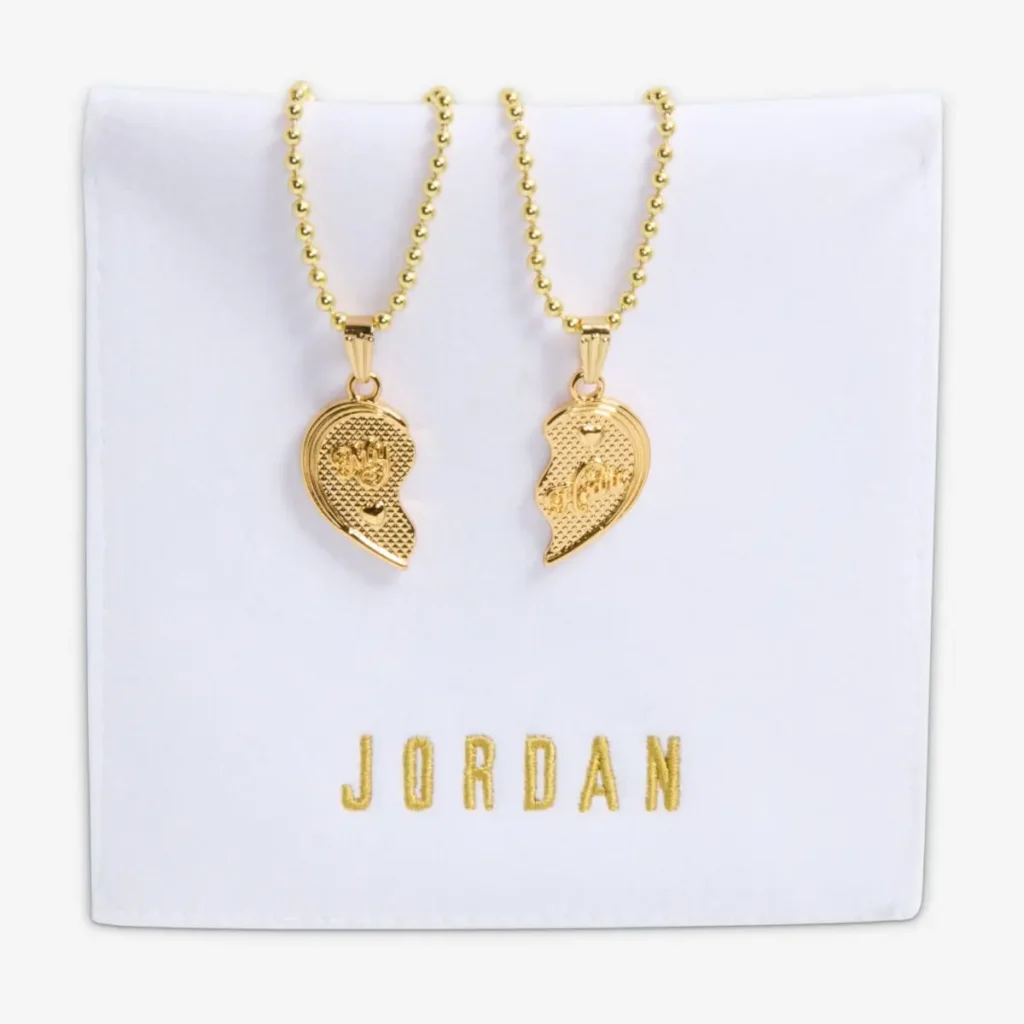 Pair of gold-tone necklaces with split heart pendants—each half engraved with “Best” and “Friends”—hanging from ball chains, displayed on a white pouch embroidered with “JORDAN” in gold lettering