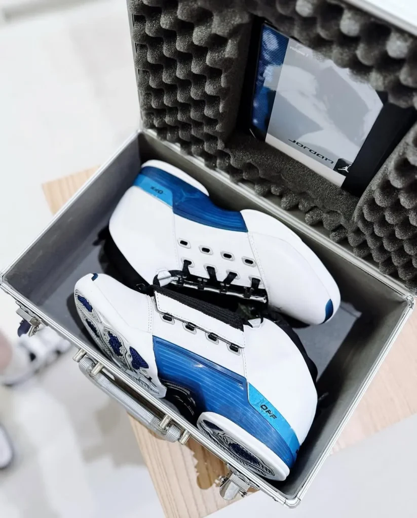 Air Jordan 17 “College Blue” shoe placed inside signature metal briefcase with foam interior, showing white leather uppers, blue gradient midsoles, black shrouds, and included CD packaging