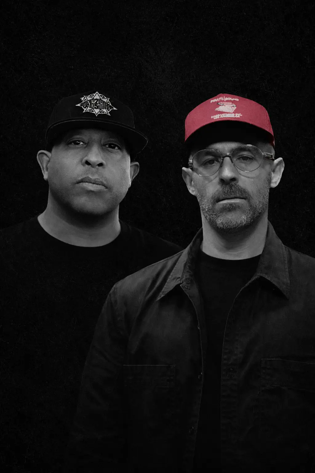 Dj Premier left side as right side The Alchemist standing side by side against a dark textured background, both wearing caps and facing forward with neutral expressions; one wears glasses and a jacket while the other wears a tee