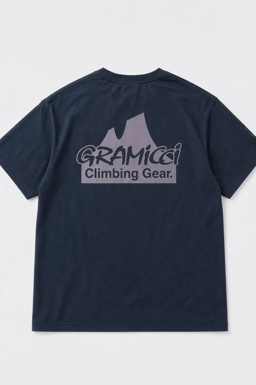 High-resolution back view of a navy Gramicci T-shirt laid flat, featuring a centered mountain-shaped graphic with the “Gramicci Climbing Gear” logo printed across the upper back on a clean studio background