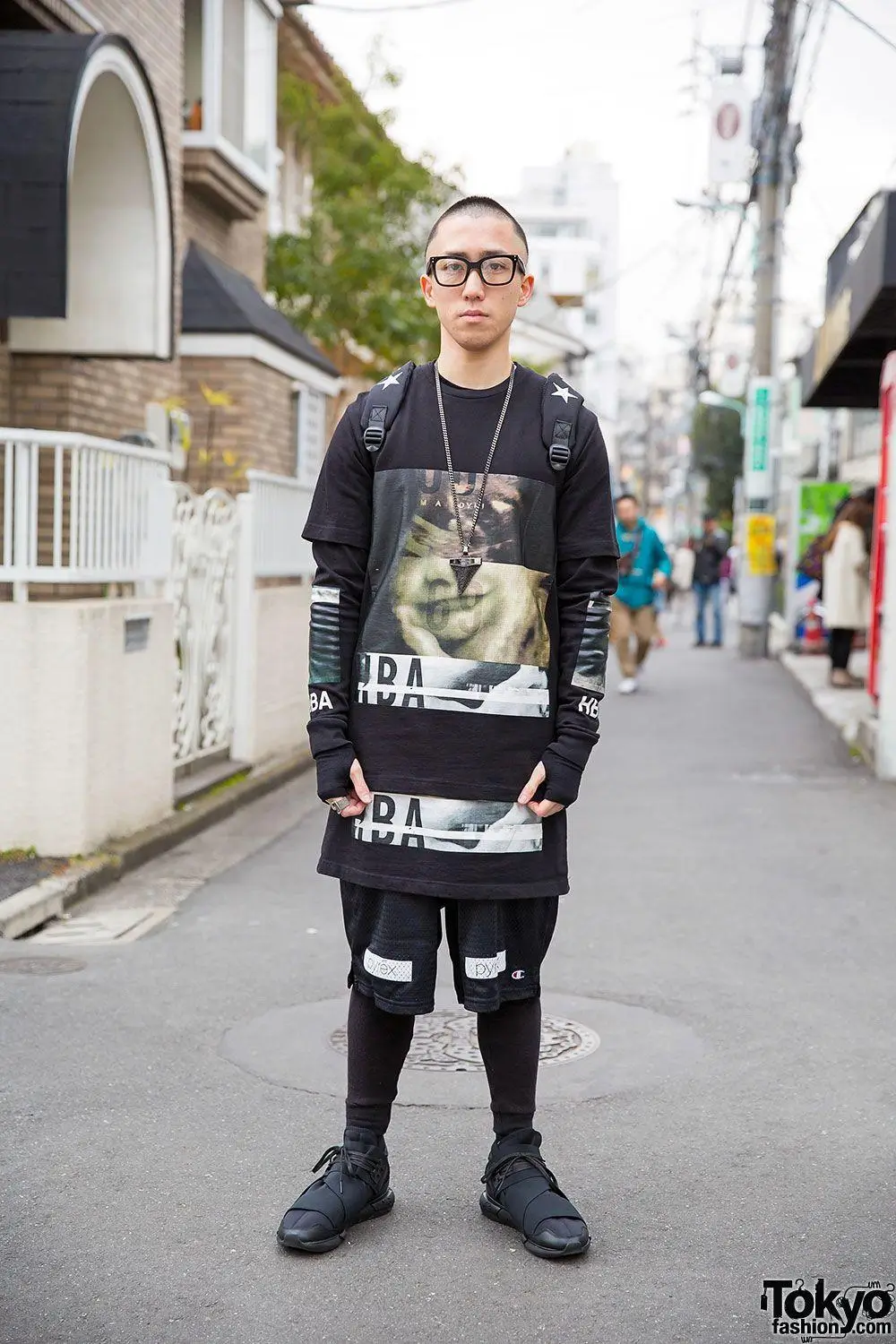 Tokyo street style featuring a sharp buzz-cut guy in layered black graphic long-sleeve, mesh shorts, and minimalist sneakers. Clean, modern skate-meets-streetwear aesthetic