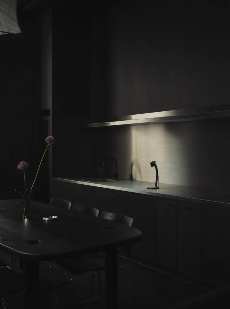 Minimalist kitchenette area in Spotify’s London Listening Lounge featuring dark cabinetry, stainless steel surfaces, and a softly lit acoustic interior
