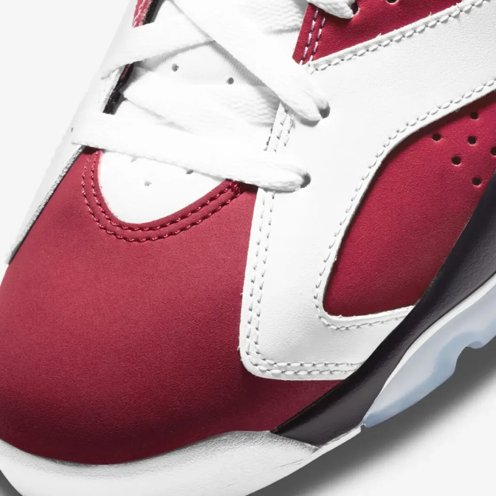 Close-up detail of the Air Jordan 6 “Carmine” showing red nubuck panels, white leather overlays with visible stitching, perforations, and textured laces above the midsole edge
