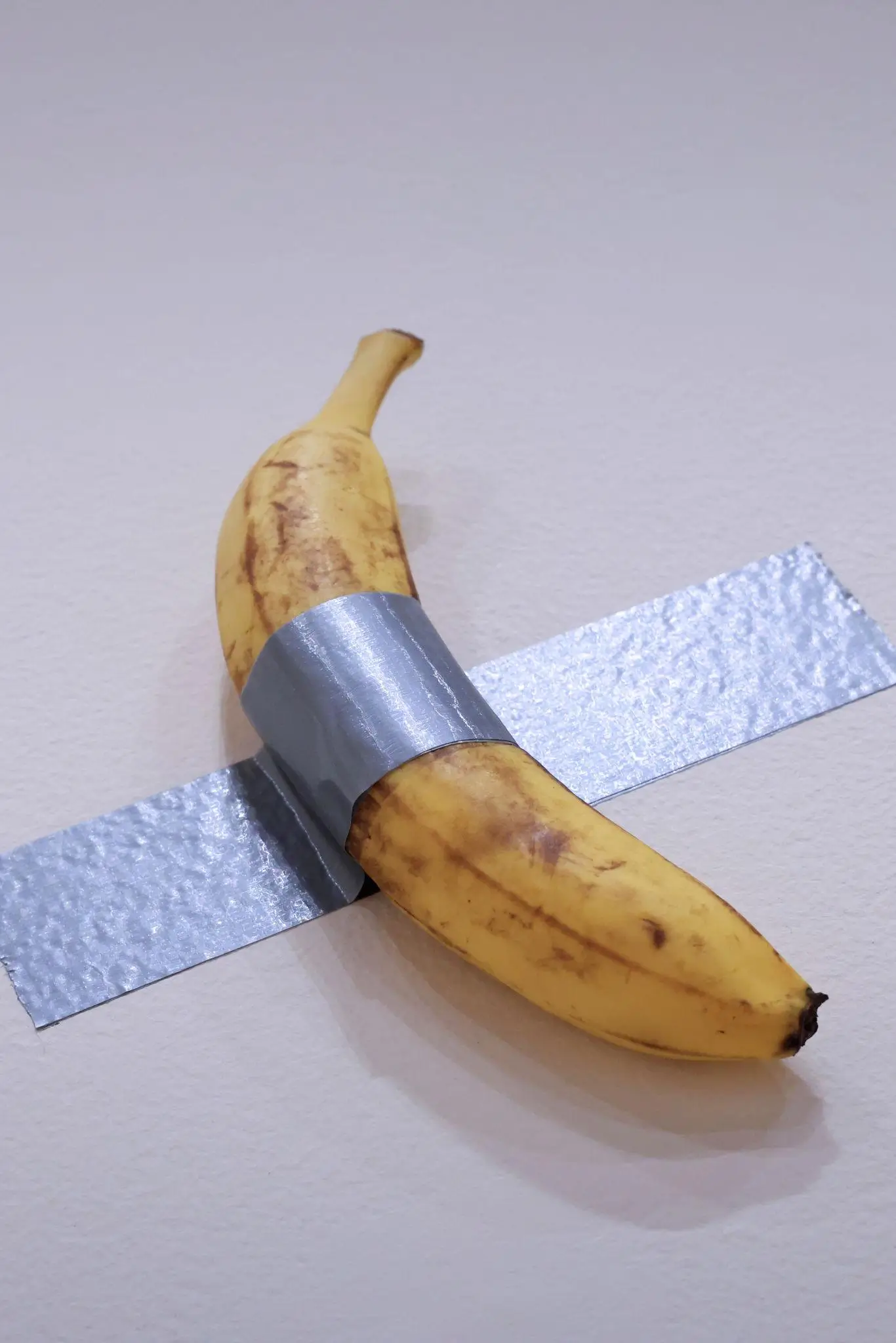 Conceptual artwork by Maurizio Cattelan featuring a ripe banana duct-taped to a gallery wall, illustrating his provocative and satirical approach to contemporary art and value systems