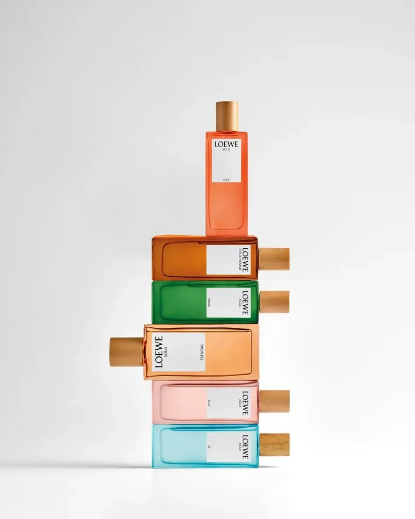 Stacked Loewe Solo Ella and Esencia perfume bottles in vibrant orange, green, pink, and blue gradient glass arranged in a sculptural vertical composition with wooden caps