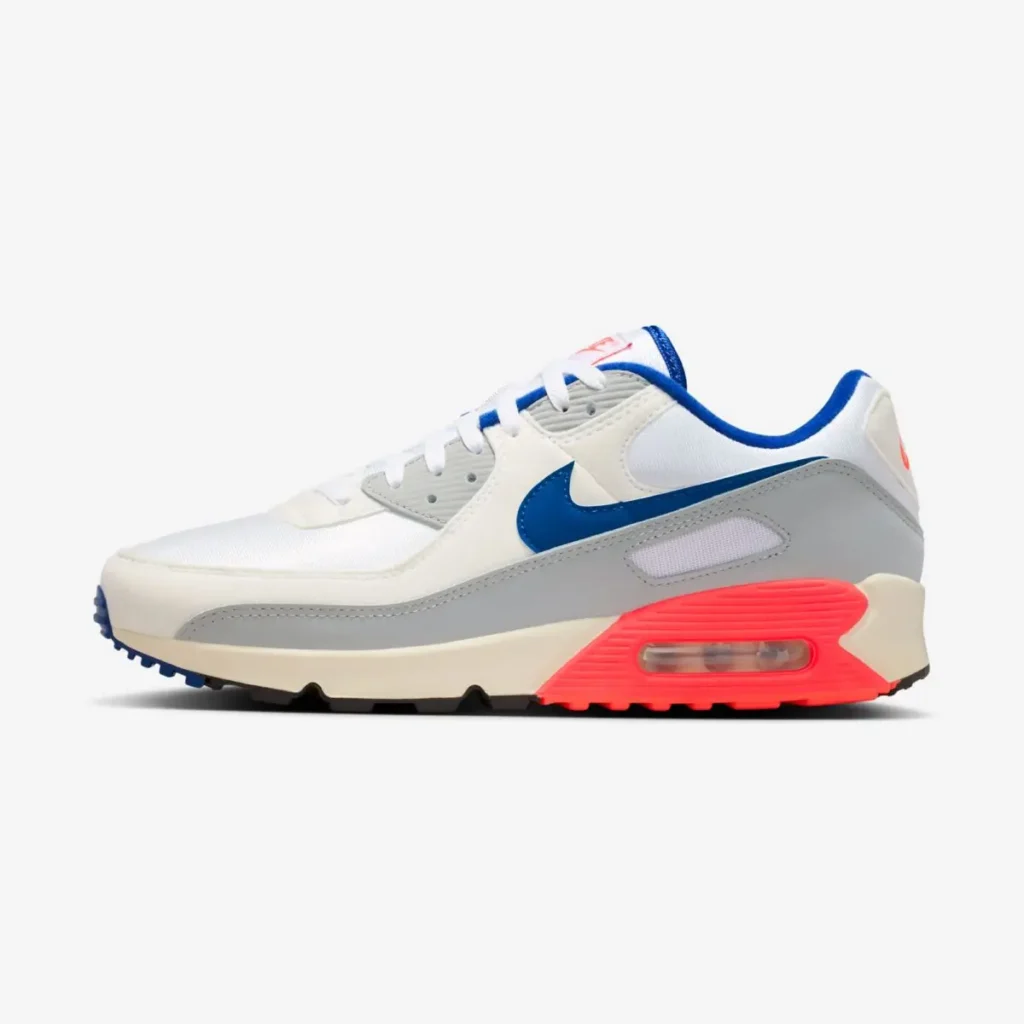 Nike Air Max 90 “Ultramarine” shoe in white mesh with light grey overlays, featuring a blue Swoosh and bright red accent around the visible Air unit on the midsole, shown in lateral side profile on a clean background
