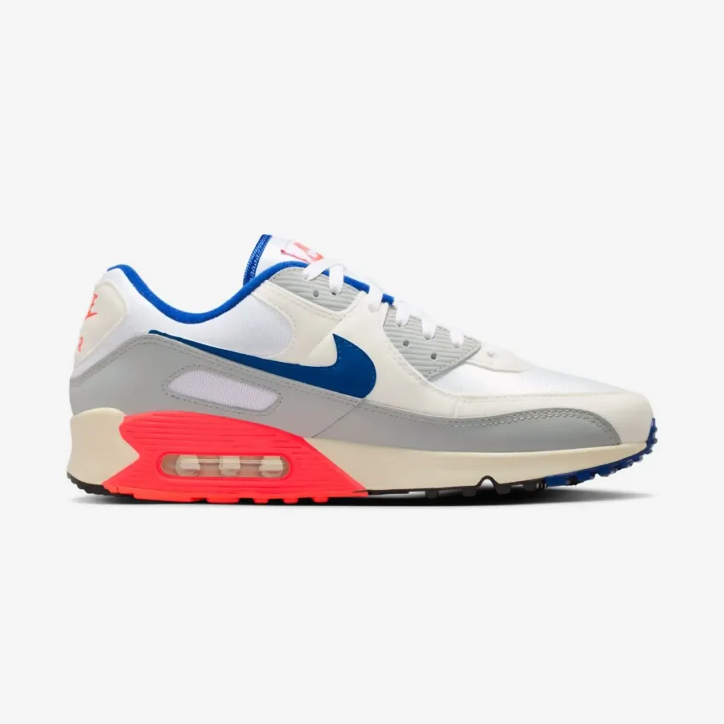 Nike Air Max 90 “Ultramarine” shoe shown in lateral side profile, featuring a white mesh upper with light grey and off-white overlays, a blue Swoosh, and a vivid red-accented midsole with visible Air cushioning against a clean background