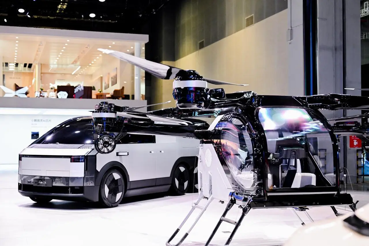 Futuristic electric concept vehicle displayed alongside a compact passenger drone at Auto China 2026, featuring exposed rotor blades, transparent cabin design, and a minimalist EV with geometric styling in a high-tech exhibition setting