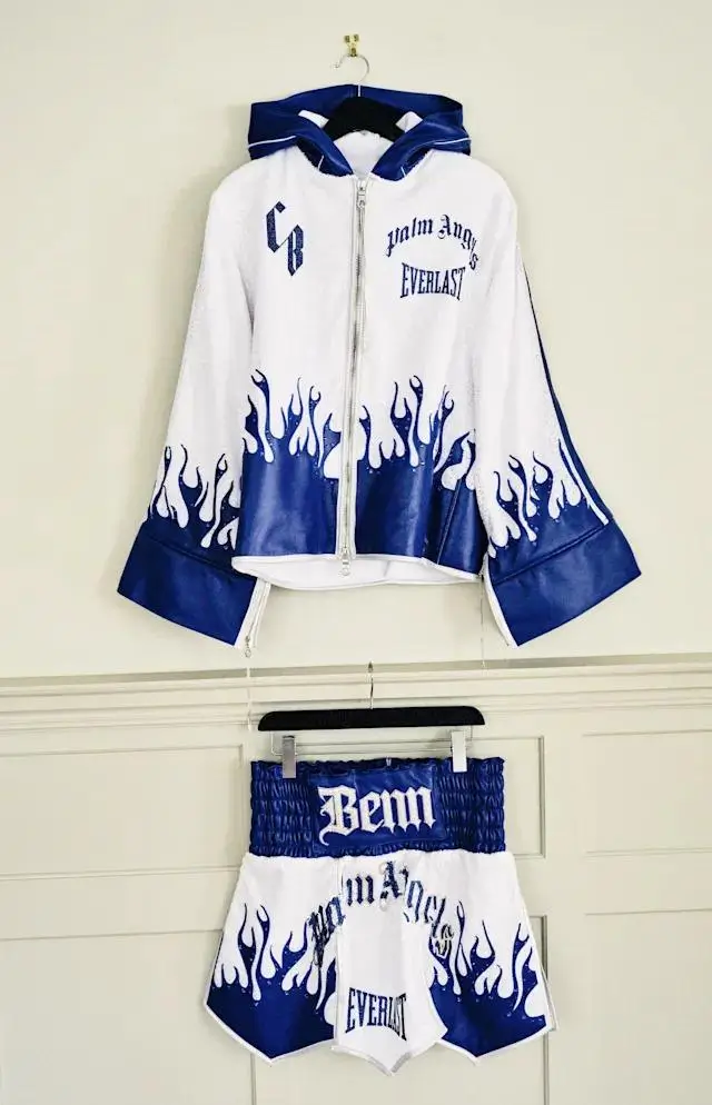 Everlast × Palm Angels boxing robe and trunks set in white and blue with flame graphics, featuring “Benn” waistband branding and gothic-style lettering on a hanging display