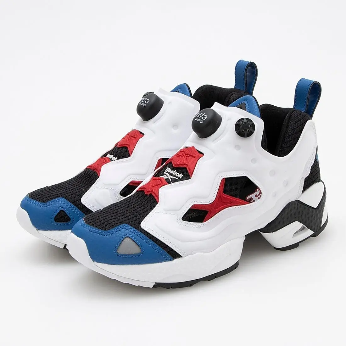 A pair of Reebok Instapump Fury shoe displayed against a clean white background, featuring a bold white cage overlay with the signature Pump inflation buttons on the tongue. The upper combines black mesh with vivid red structural accents and blue panels at the toe and heel, while the chunky segmented sole includes black and white cushioning elements, emphasizing the model’s iconic, futuristic design
