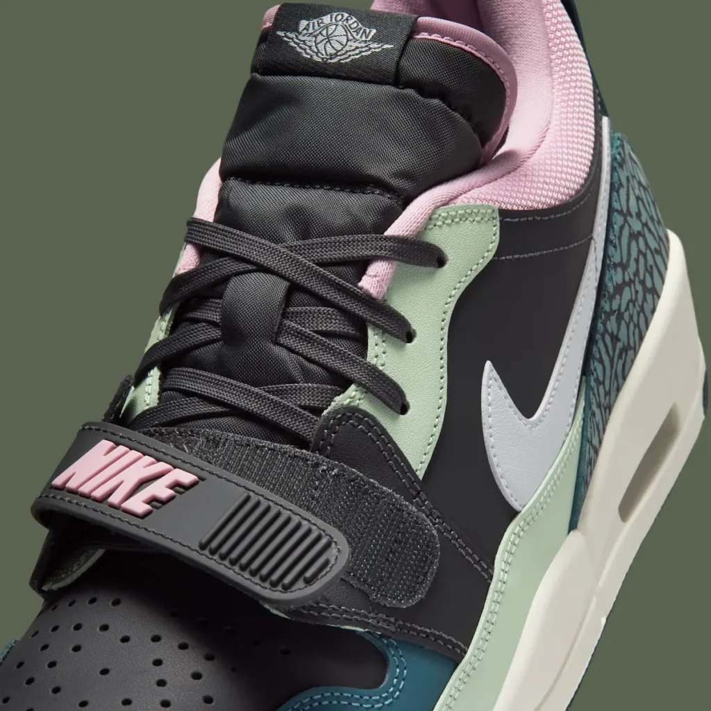 A close-up product image of a Nike Air Jordan shoe, highlighting its layered construction and mixed-material design. The shoe features a black base with pastel accents—mint green panels, a pink inner lining, and a teal elephant-print heel wrap. A white Nike Swoosh contrasts against the dark upper, while black laces sit over a padded tongue with the Air Jordan Wings logo. The forefoot strap, embossed with “NIKE” in soft pink, adds a retro basketball aesthetic, and the visible Air unit in the midsole reinforces its heritage performance roots