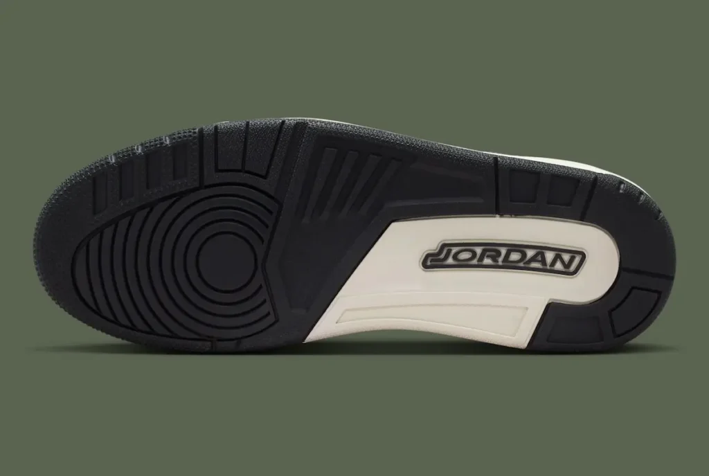A bottom view of a Nike Air Jordan shoe outsole, showcasing its traction pattern and branding. The sole is primarily black with a mix of circular pivot points at the forefoot and linear grooves for grip and flexibility. A contrasting off-white midfoot section features embossed “JORDAN” branding, adding a bold visual break. The textured rubber construction emphasizes durability and court-inspired performance design