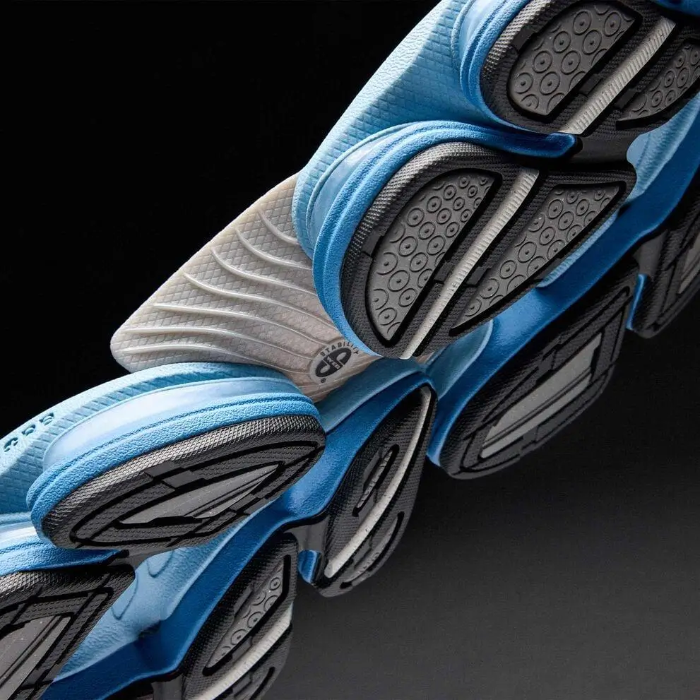 Close-up of stacked light blue athletic shoe showing detailed black rubber soles and white midsoles against black background