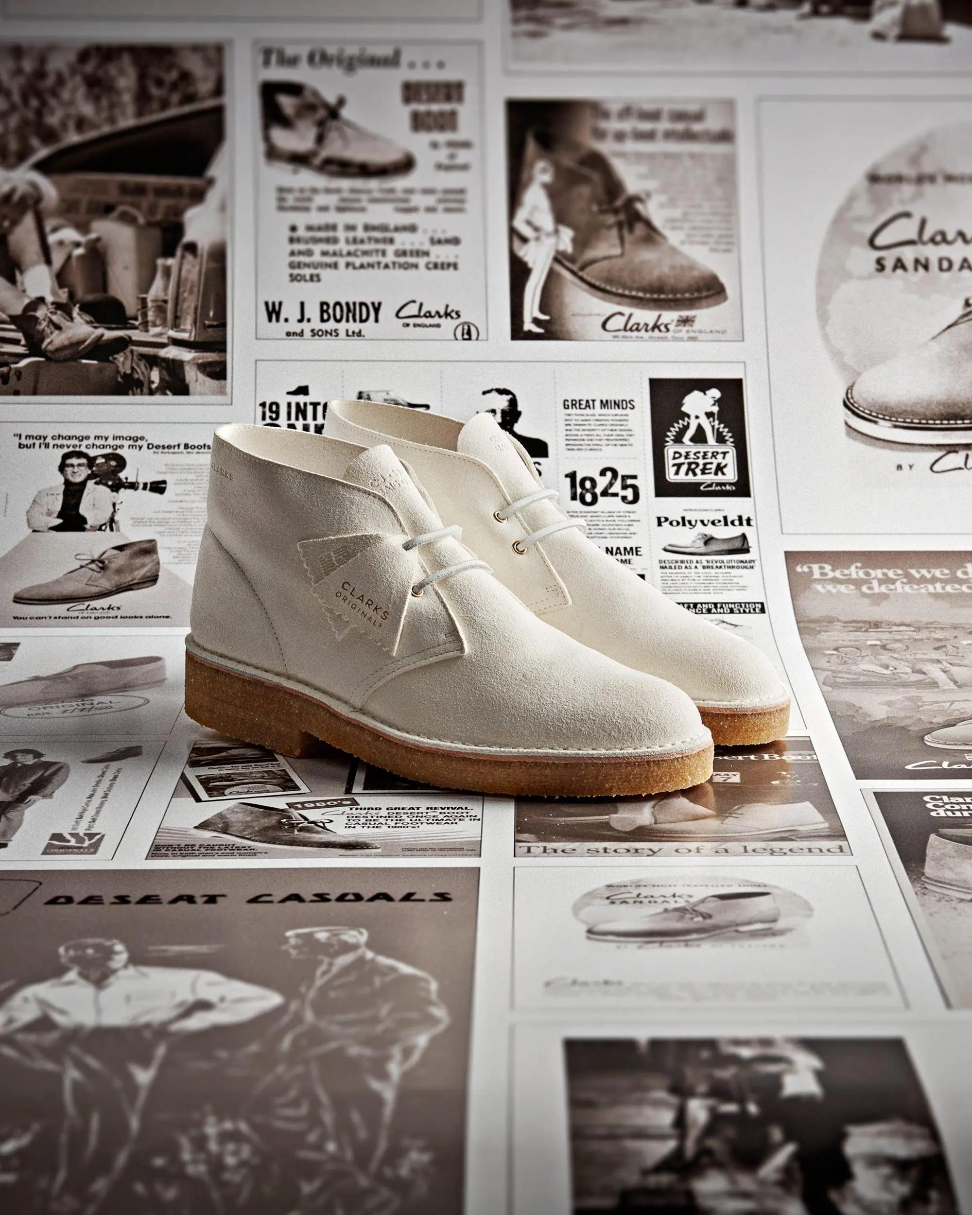 Cream suede Clarks Originals Desert Boot with a clean two-eye lace design and crepe sole, presented atop a collage of vintage Clarks advertisements and archival imagery