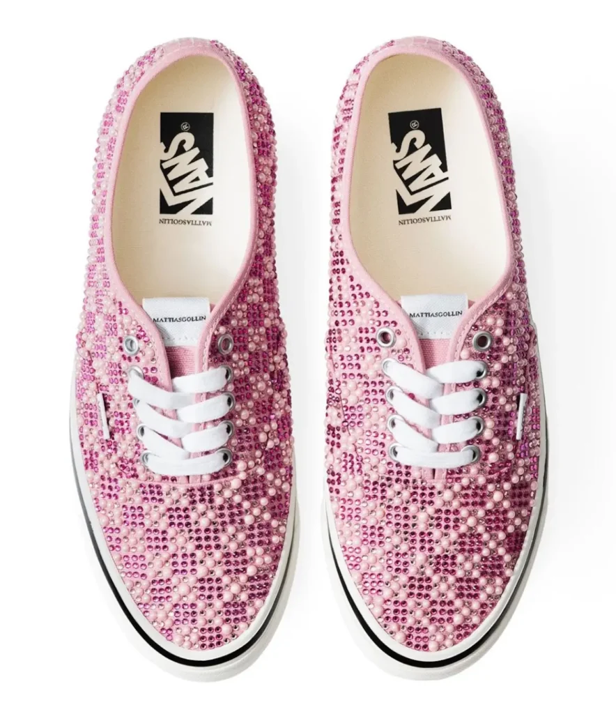 Top-down view of a pair of pink Vans Authentic shoe densely covered in rhinestones and pearl-like studs, featuring white laces, silver eyelets, and visible Mattias Gollin branding on the tongue and insole