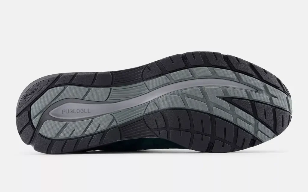 Bottom view of a New Balance shoe highlighting the outsole design, featuring a segmented tread pattern in dark rubber for traction and durability. The midfoot area displays a lighter grey section with “FuelCell” branding, indicating responsive cushioning technology. Grooved flex channels run throughout the sole, enhancing flexibility and movement, while the overall layout balances grip and comfort in a performance-oriented structure