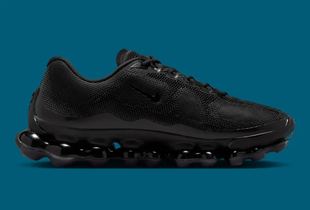 Side profile of Nike Air Liquid Max “Triple Black” shoe, showcasing the sculpted black mesh upper, minimal Swoosh detailing, and distinctive point-loaded Air pod sole with a glossy translucent black finish against a teal background