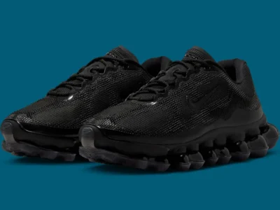 Three-quarter angled view of Nike Air Liquid Max “Triple Black” sneakers, highlighting the textured black mesh upper, tonal Swoosh, and segmented point-loaded Air pod sole with a glossy translucent finish on a teal background