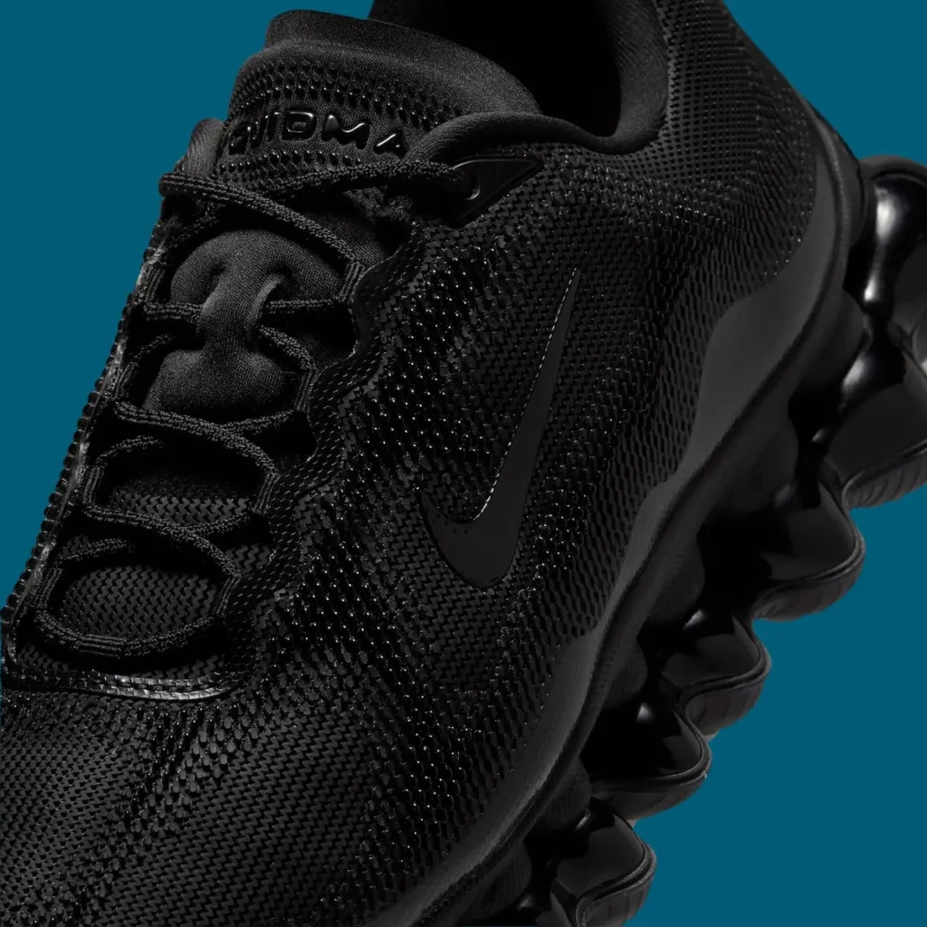 Close-up detail of Nike Air Liquid Max “Triple Black” shoe, showing the textured three-layer mesh upper, tonal black Swoosh, integrated lacing system, and sculpted Air pod cushioning along the midsole against a teal background