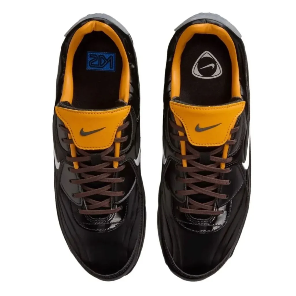 Top-down view of Nike Air Max 90 “Korea” showing glossy black leather uppers, brown laces, golden-orange padded tongues with mini Swoosh, and insole graphics including blue KR logo and triangular Nike emblem