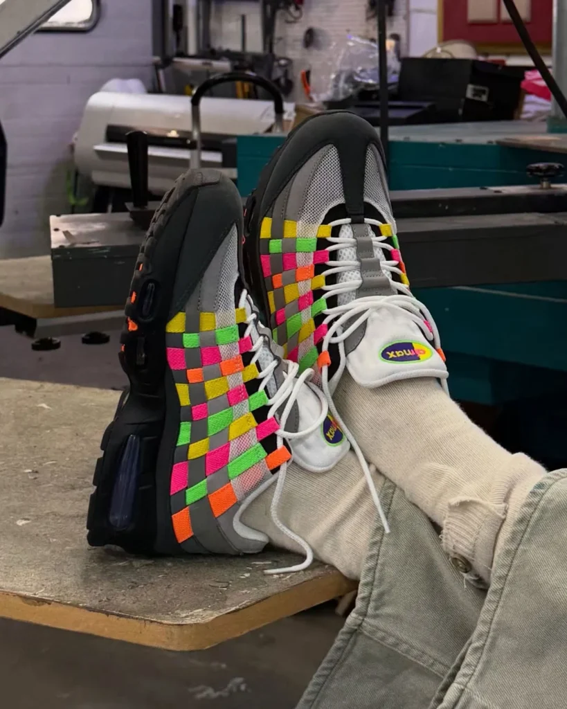 On-foot view of Nike Air Max 95 Woven “Grey/Multi” pair featuring multicolor woven upper and black midsole, worn with beige socks and green pants in a workshop setting