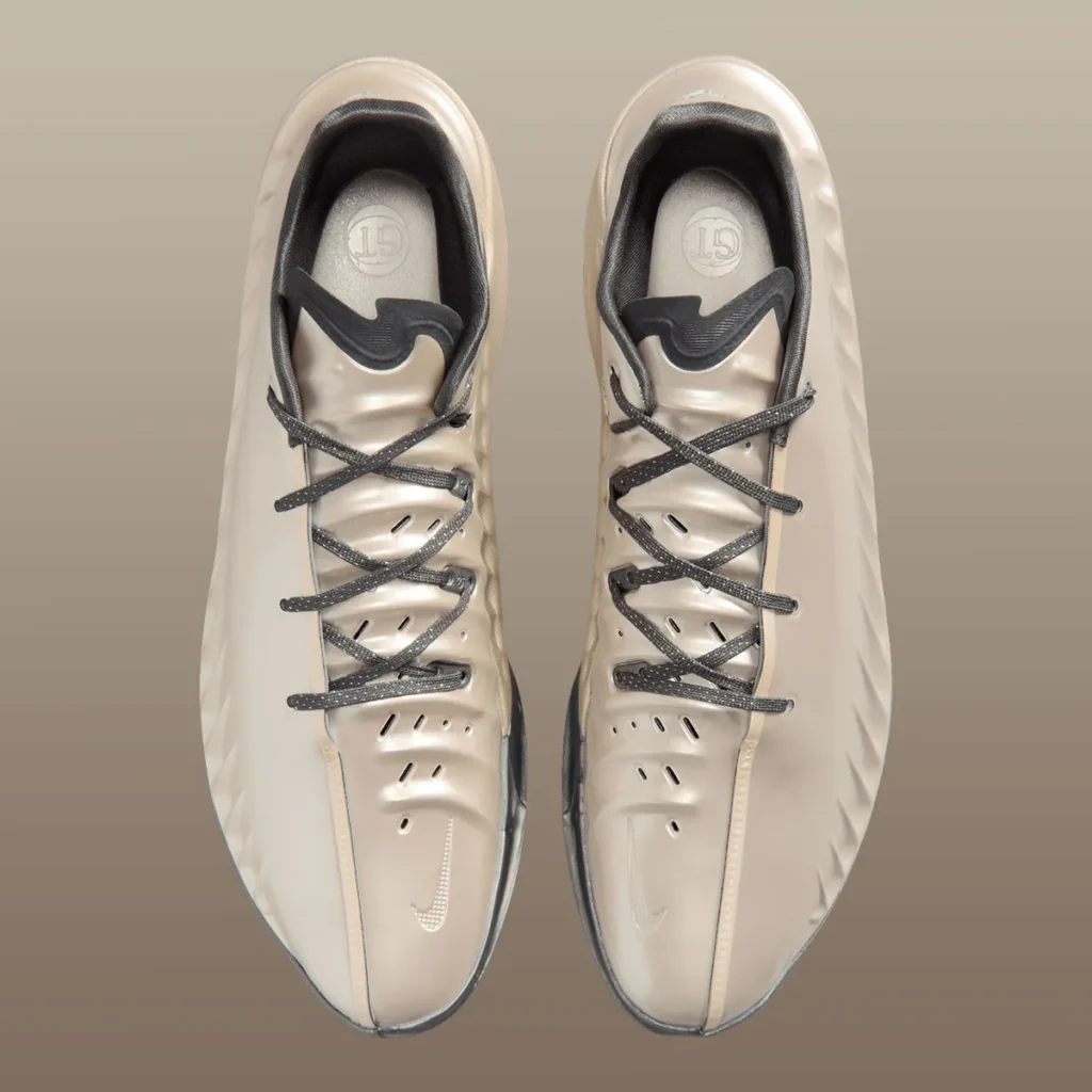 Top-down view of a pair of Nike low-top basketball shoes in a champagne-beige finish, featuring dark gray laces, perforated detailing along the forefoot, sculpted ridges on the upper, and tonal Swoosh accents on the toe, emphasizing a sleek, performance-focused design
