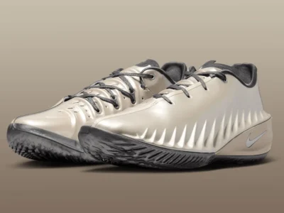 Three-quarter view of a pair of Nike low-top basketball shoes in a champagne-beige finish, featuring sculpted, ribbed uppers, dark gray laces, a streamlined midsole with subtle metallic sheen and Swoosh branding, and a smoky translucent outsole designed for grip and quick lateral movement