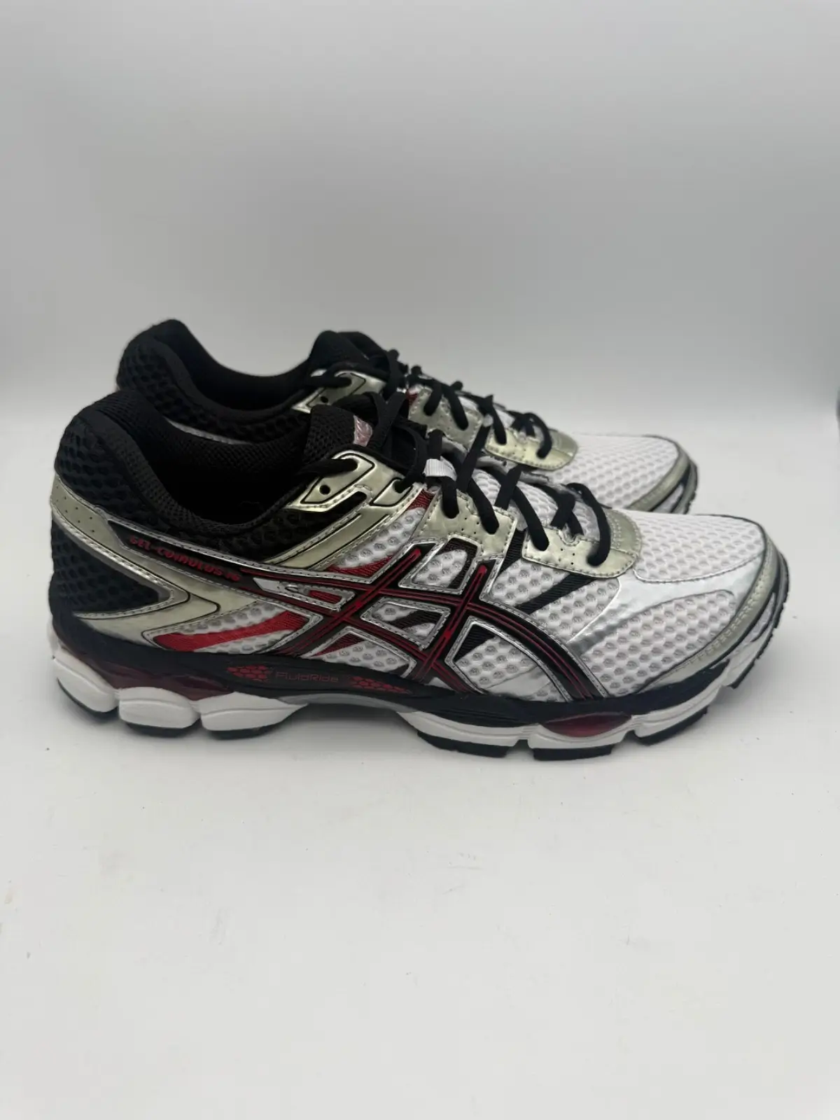 Angled side view of a pair of ASICS GEL-Cumulus running shoes in white, black, and red, featuring breathable mesh uppers, metallic silver overlays, black laces, signature ASICS side stripes, and a cushioned midsole with visible GEL inserts and FluidRide technology branding