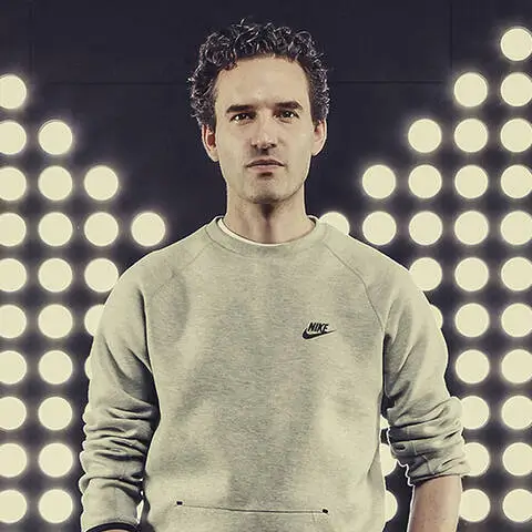 Martin Lotti, standing front-facing in a minimalist studio, wearing a light grey Nike sweatshirt, with symmetrical circular studio lights glowing behind him, creating a clean, high-contrast, modern athletic aesthetic