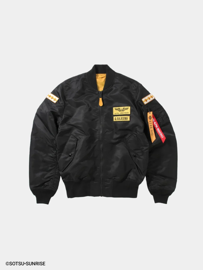 Black MA-1 bomber jacket shown from the front with a slightly glossy nylon finish and ribbed collar, cuffs, and hem. The design features gold embroidered chest patches reading “Alpha Industries” and “Q. Bajeena,” matching three-star sleeve patches on both arms, and a sleeve utility pocket with red “Remove Before Flight” and yellow A.E.U.G. tags, with a hint of yellow lining visible at the collar