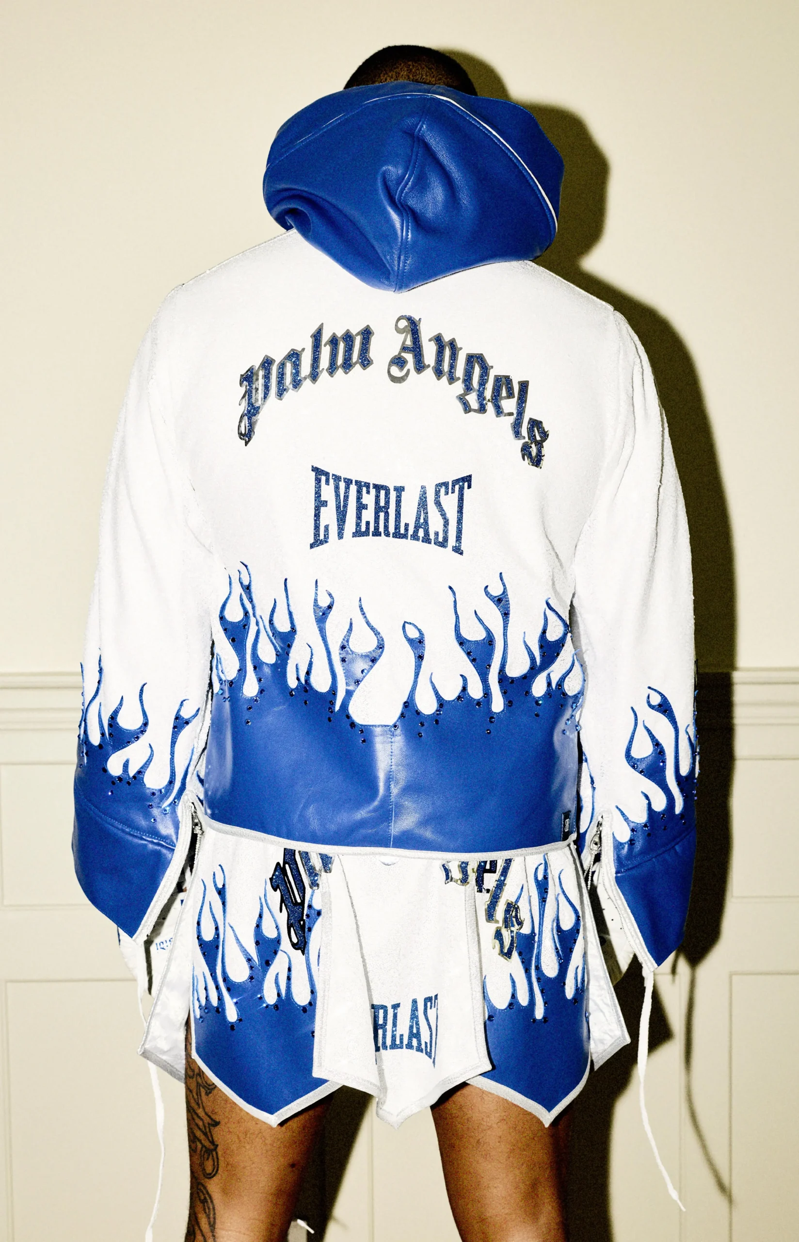 Back view of Everlast × Palm Angels boxing robe and trunks in white and blue with flame graphics, featuring “Palm Angels” and “Everlast” branding and crystal embellishment detailing