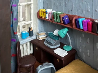 Handcrafted miniature writer’s room with a desk, vintage typewriter, bookshelves, lamp, chair, and window overlooking a tiny apartment interio