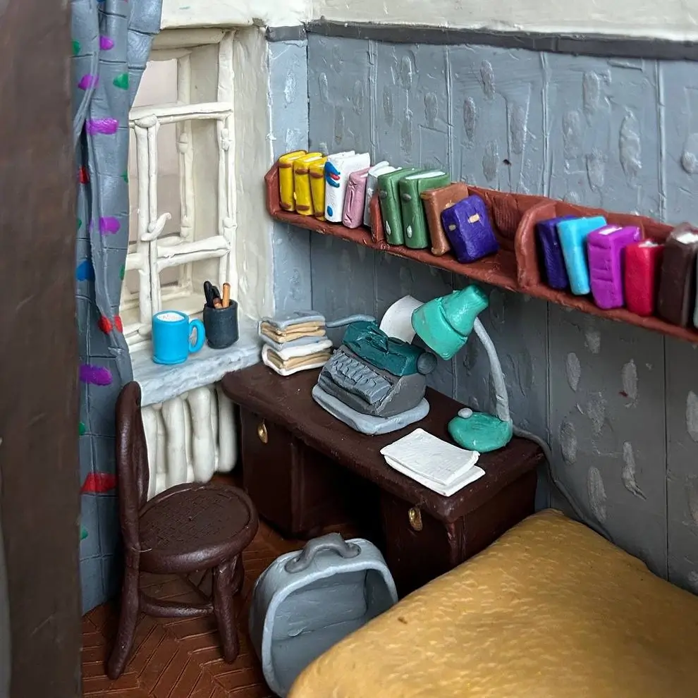 Handcrafted miniature writer’s room with a desk, vintage typewriter, bookshelves, lamp, chair, and window overlooking a tiny apartment interio