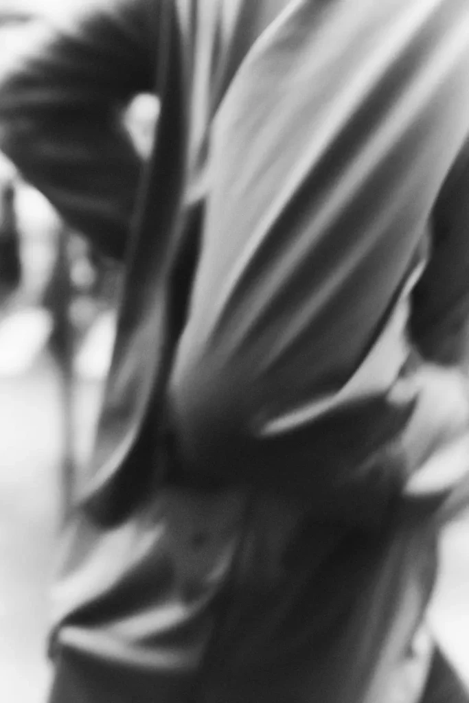 Abstract black-and-white motion-blurred close-up of runners in lightweight technical apparel, emphasizing fabric movement, speed, and the atmospheric rhythm of a group run through soft-focus urban surroundings