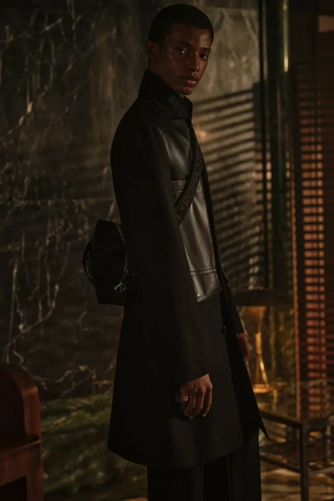 Portrait of a model in a black leather-paneled overcoat with a crossbody Fendi bag, photographed in warm shadow lighting inside a luxurious marble setting