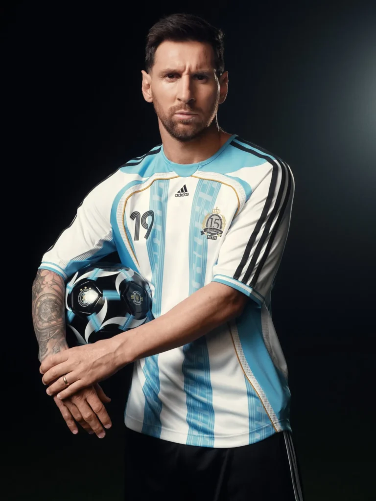 Studio portrait of a football player in a white and sky-blue striped jersey holding a dark graphic football under one arm, standing against a black background with dramatic lighting