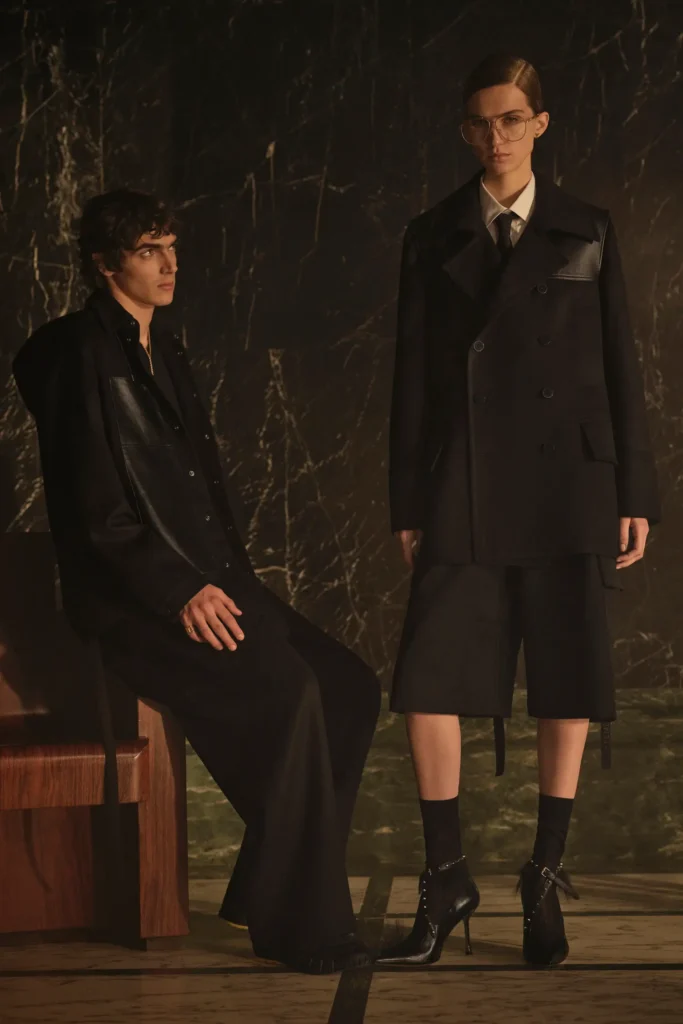 Two models dressed in coordinated black Fendi tailoring and elongated silhouettes, blending structured outerwear with minimalist gothic elegance and polished leather accents