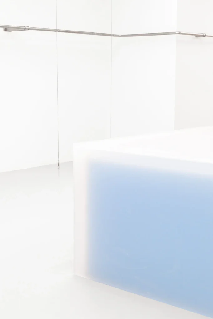 Minimalist retail interior detail featuring a glowing translucent cube display with soft blue illumination, set against clean white panel walls and suspended metal clothing rails