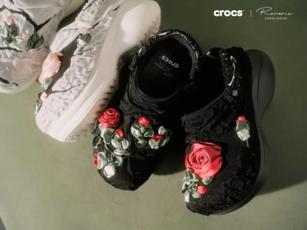 Black and ivory Crocs x Caroline Hú Bae Clogs featuring oversized hand-crafted ribbon roses and textured floral detailing in editorial product style