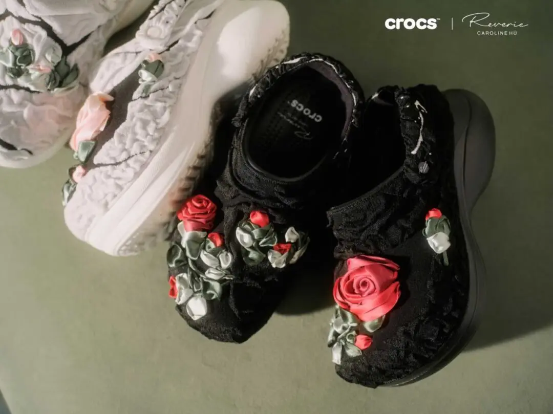 Black and ivory Crocs x Caroline Hú Bae Clogs featuring oversized hand-crafted ribbon roses and textured floral detailing in editorial product style