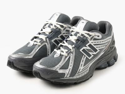Pair of New Balance 1906R shoe in dark grey mesh with metallic silver overlays, photographed from a front three-quarter angle to showcase the technical running-inspired design, cream laces, and chunky cushioned sole