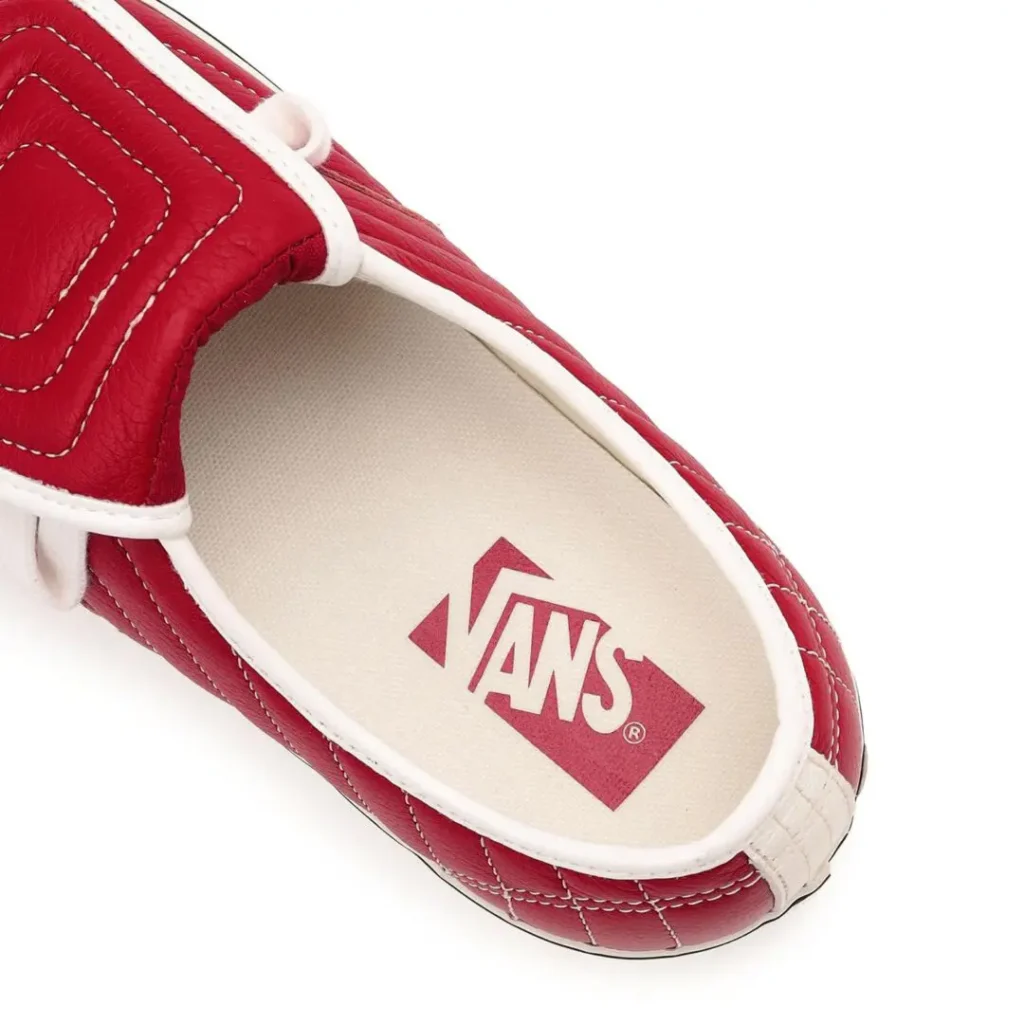 Close-up overhead detail of the interior of a red quilted Vans shoe, revealing cream canvas lining, red Vans footbed logo, textured leather upper, and padded tongue construction