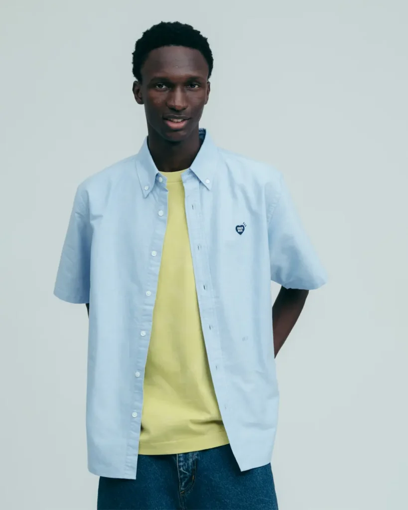 Studio portrait of a model wearing a light blue Human Made button-up shirt layered over a pastel yellow tee with relaxed denim style