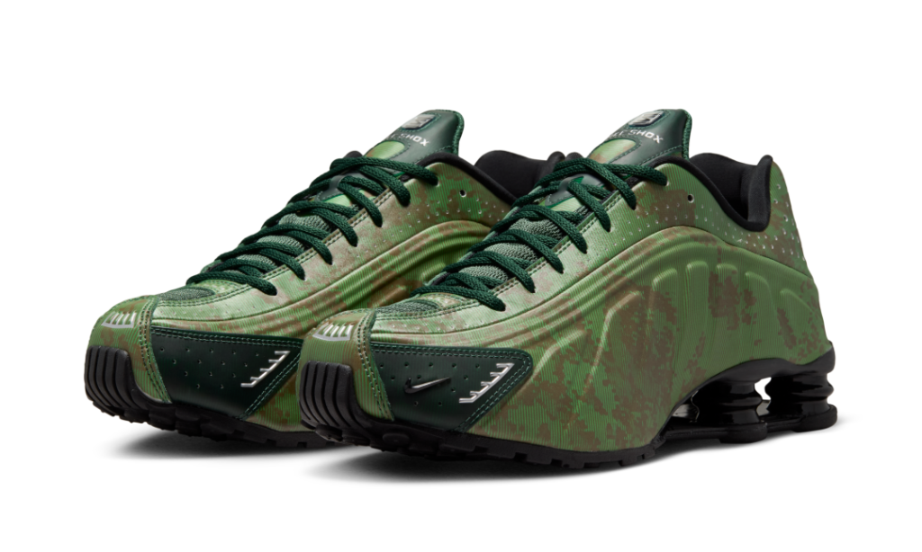 Nike Shox R4 “Noble Green/Team Kelly Green” shown as a pair in a three-quarter angle, featuring layered green graphics across the molded upper, dark forest green laces, reflective accents, and glossy black Shox columns