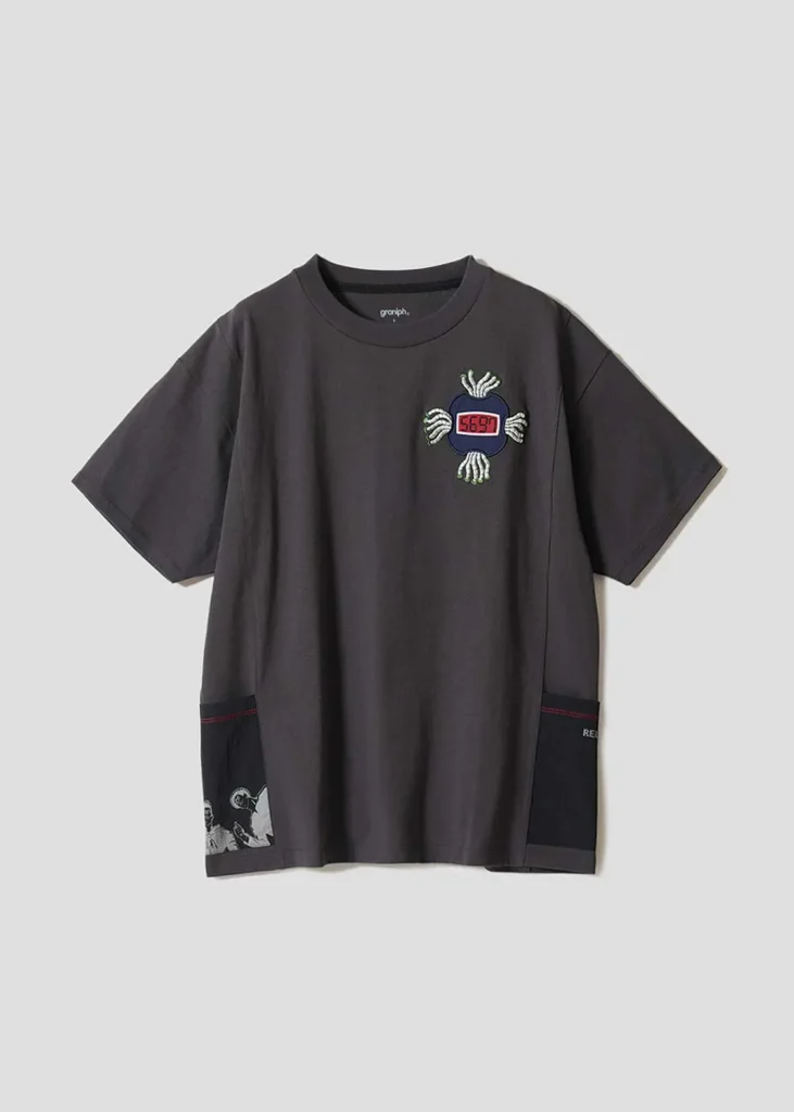 Dark charcoal graphic T-shirt featuring an embroidered digital-style emblem at the chest with contrast utility-inspired panel detail