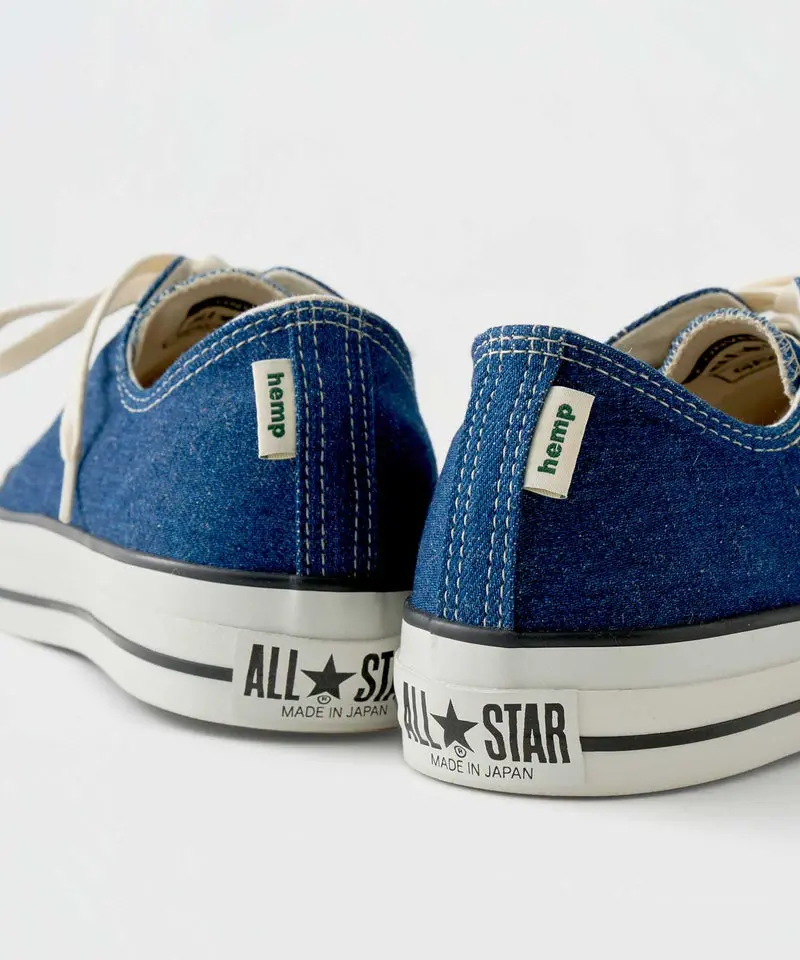 Close-up rear-angle image of the Gramicci x Converse “All Star Made in Japan” shoe highlighting the textured indigo hemp uppers and detailed contrast stitching. Small woven “hemp” tags sit near the heel seams, while the classic white rubber midsoles feature bold “ALL★STAR Made in Japan” branding in black. The clean studio lighting and cropped composition emphasize the sneaker’s premium craftsmanship, sustainable material focus, and vintage-inspired Japanese production aesthetic