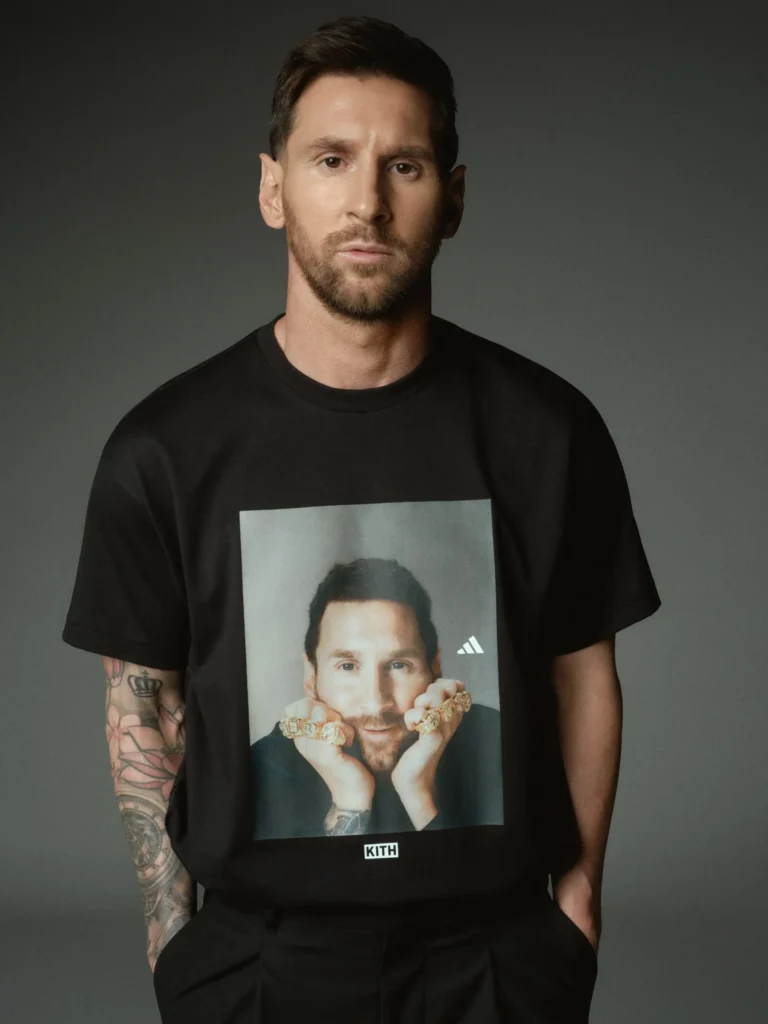 Minimal editorial portrait of a football player in a black graphic T-shirt featuring a printed portrait design, photographed against a neutral studio backdrop