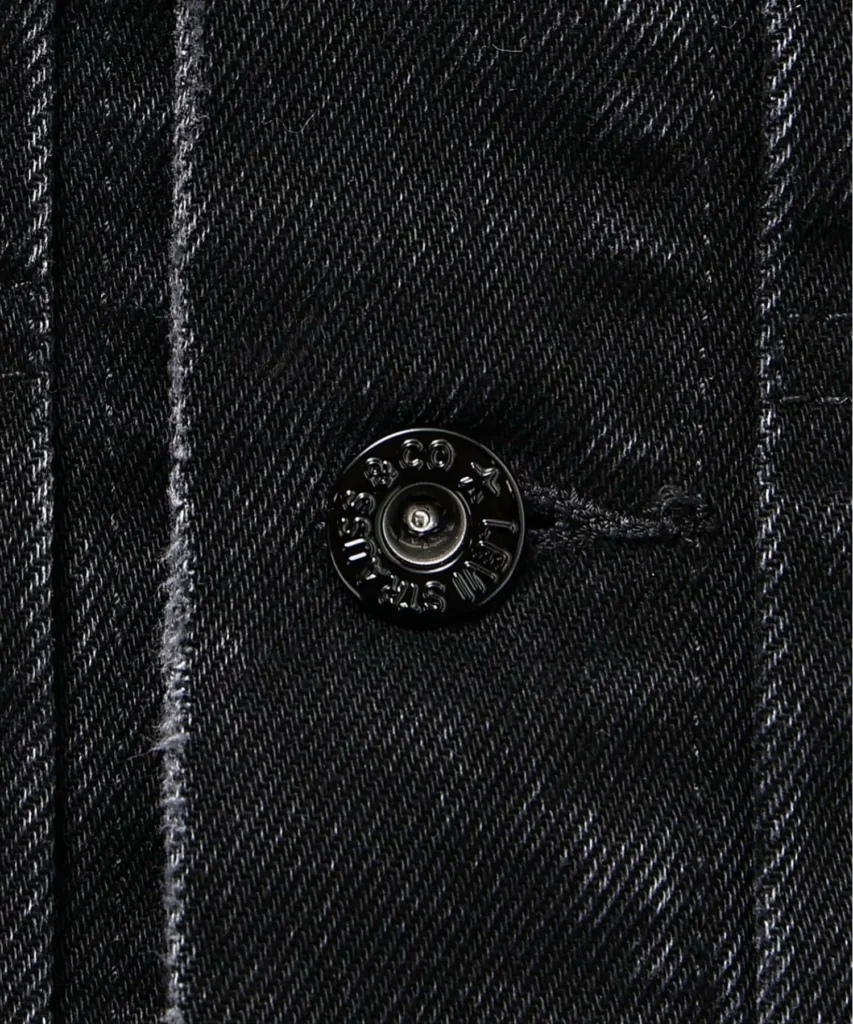 Macro shot of a black Levi’s branded metal button set against textured washed black denim on the Type II-inspired jacket