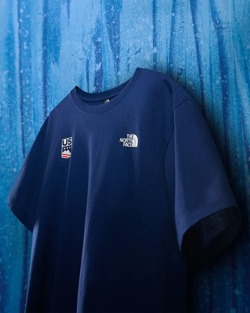 Royal blue Team USA T-shirt by The North Face displayed against an icy textured backdrop, featuring minimalist white branding and official U.S. Ski & Snowboard insignia
