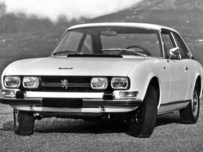 Vintage Isuzu 117 Coupé prototype displayed in black-and-white promotional photography, highlighting Giorgetto Giugiaro’s original quad-headlight front fascia, elegant grand touring proportions, and timeless Japanese-Italian design heritage